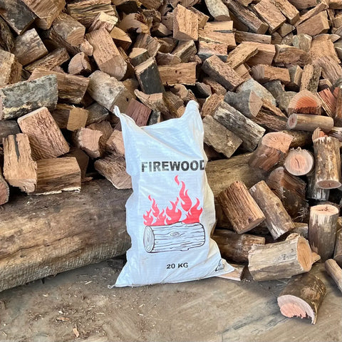 20Kg Bag Mixed Hardwood firewood bag displayed in front of stacked firewood logs.